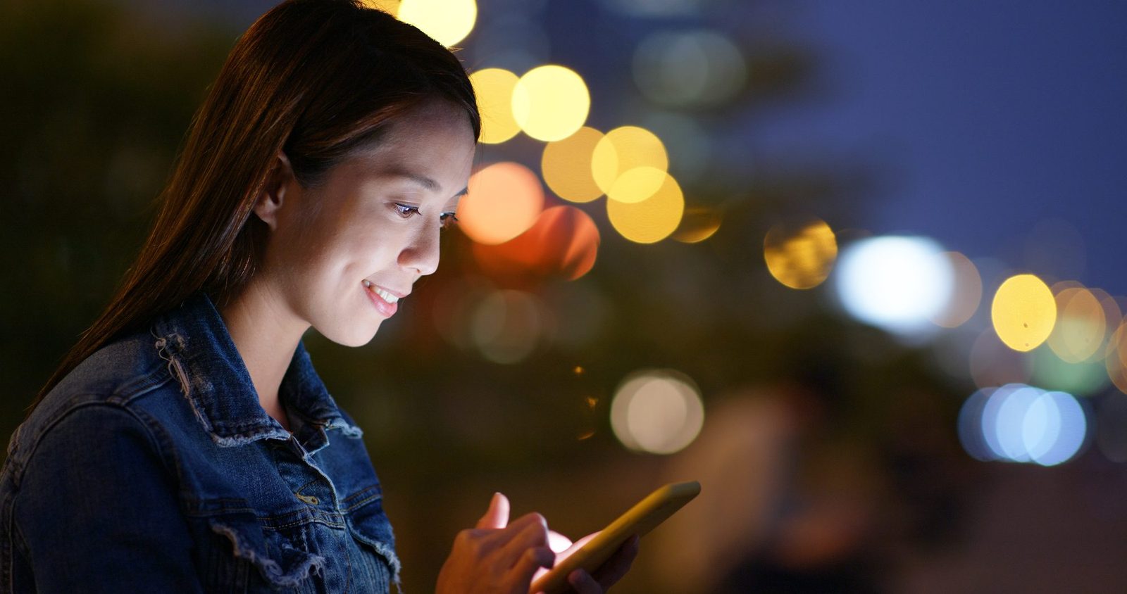 A woman using a phone alone in a city at night