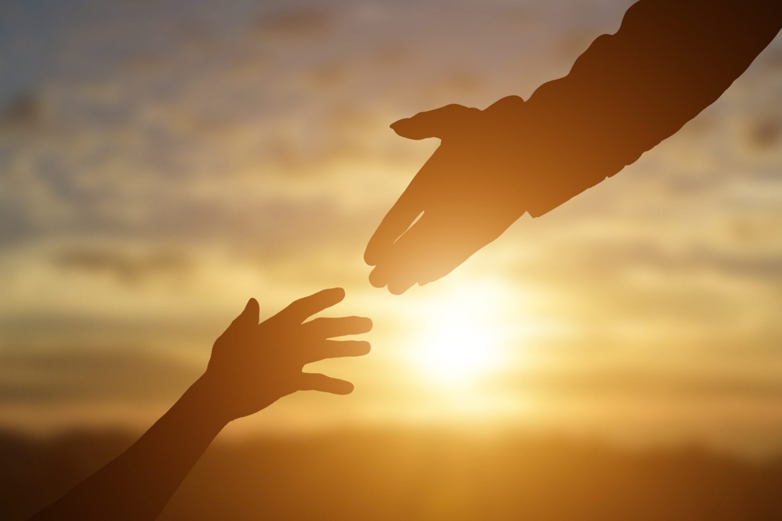 Silhouettes of people reaching out to help one another at sunset