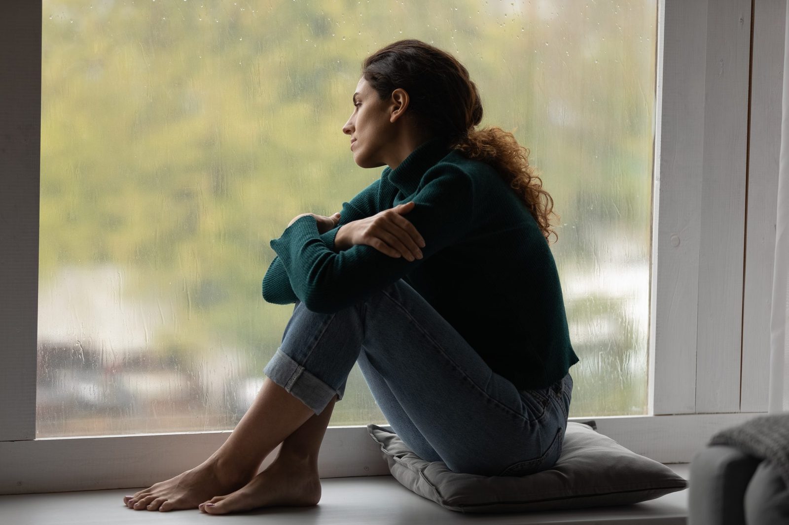A young woman sitting on a windowsill looking into the distance